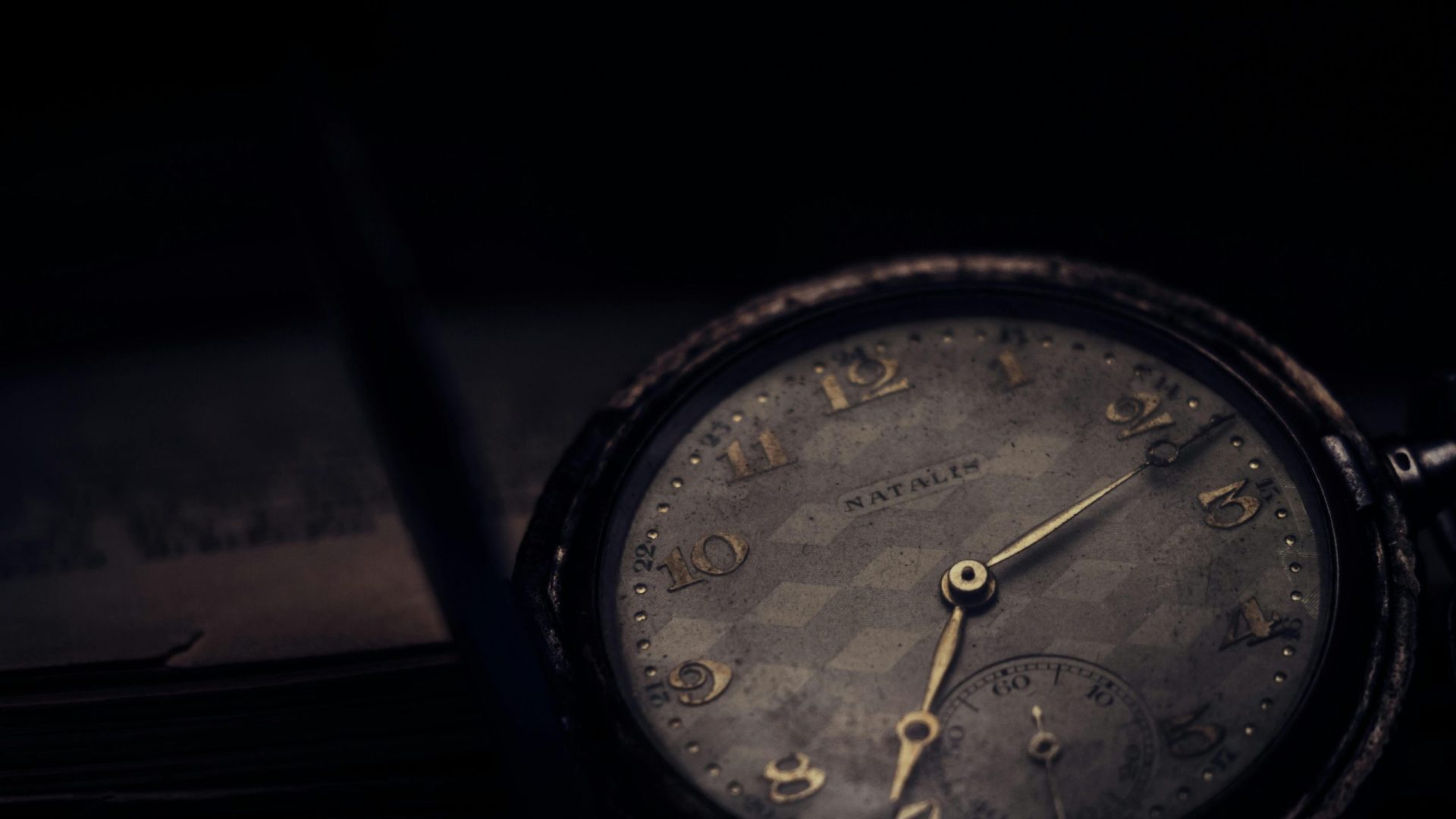 Close-up of a vintage pocket watch with a textured dial in a moody setting.